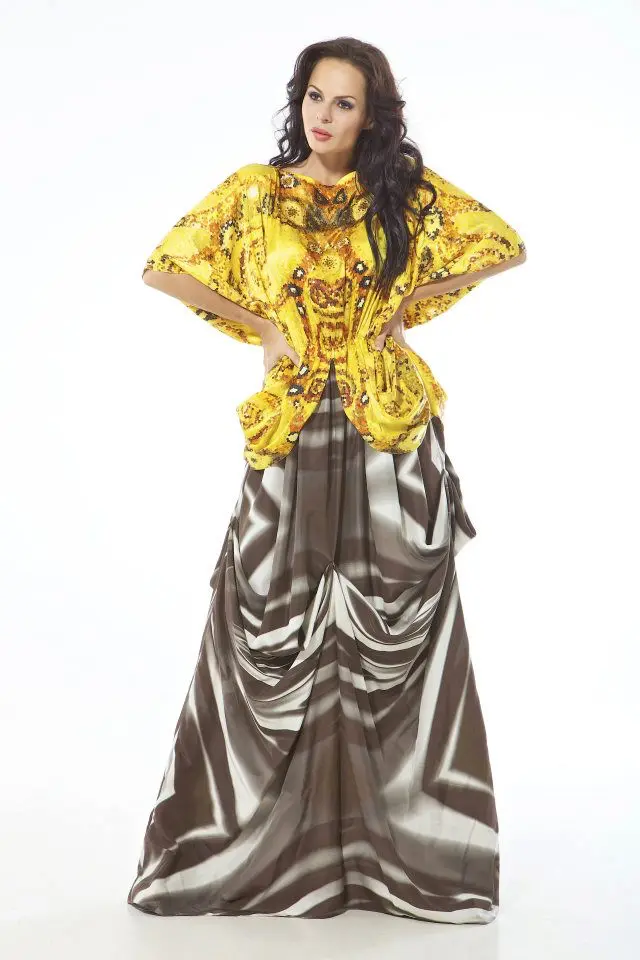Model wearing a mixed-print silk kaftan with a gold spiral motif on the top and grey-white camouflage drape from the gathered waist downward.
